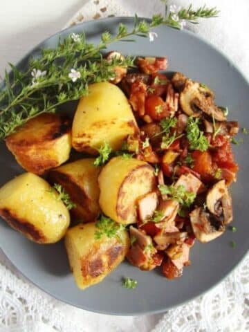 large pieces of roasted gypsy potatoes with ham sauce and fresh herbs on a grey plate.