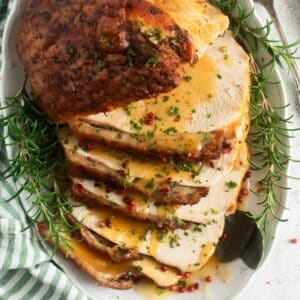 slow-roasted turkey breast sliced on a platter and sourrouded by rosemary sprigs.
