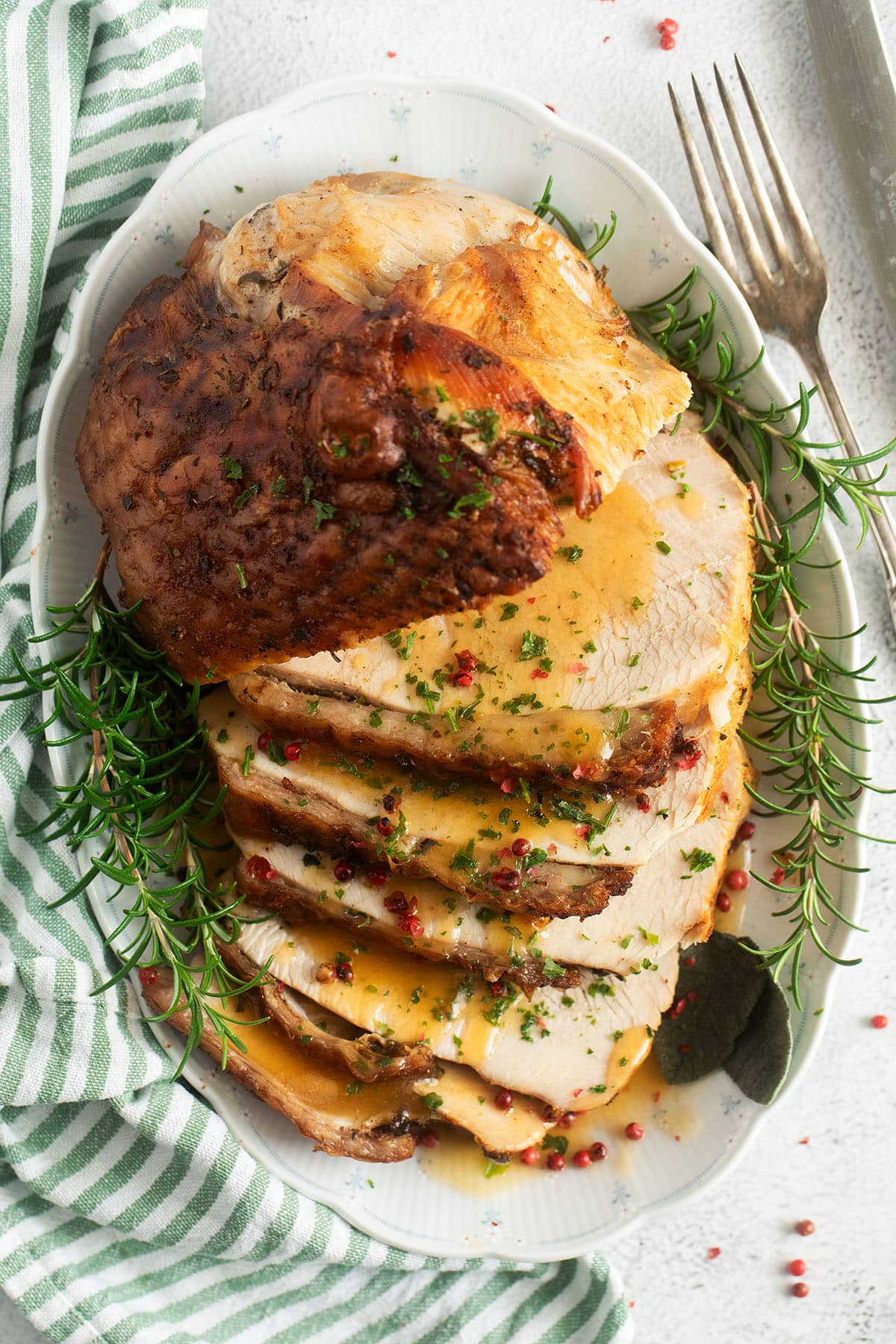 sliced turkey breast with crispy skin and gravy on a platter with rosemary sprigs around it.