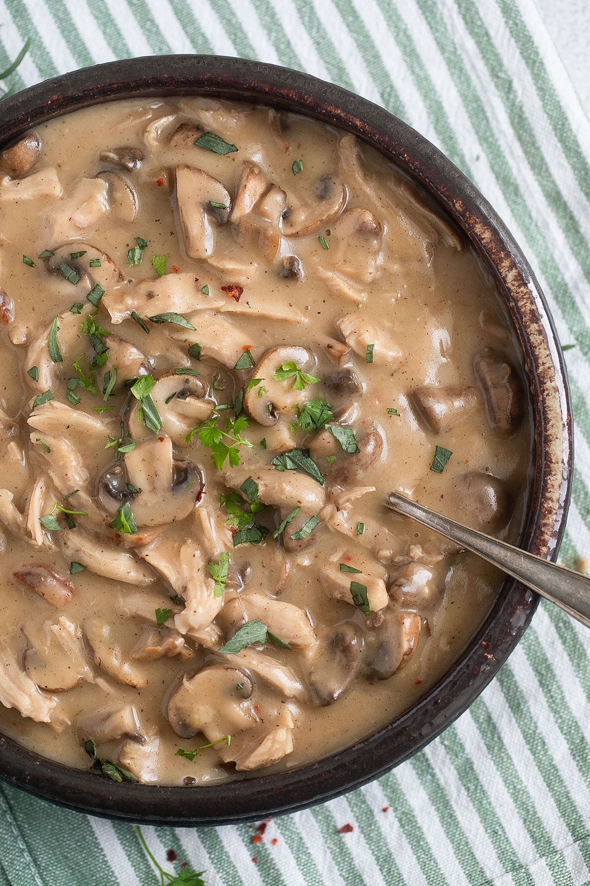 leftover turkey fricassee with mushrooms and parsley in a large serving bowl with a spoon in it. 