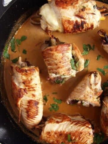 stuffed turkey roulades with sauce in a cast iron skillet.