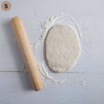 a piece of dough rolled as naan bread and a small rolling pin beside it.
