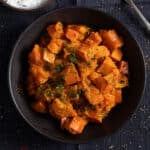 braised pumpkin pieces sprinkled with parsley and cilantro in a dark bowl.