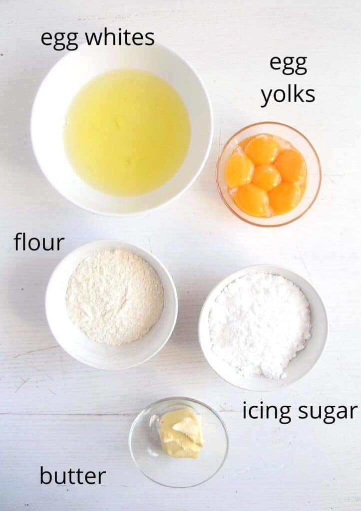 bowls with egg whites and yolks, flour, icing sugar, butter on the table.