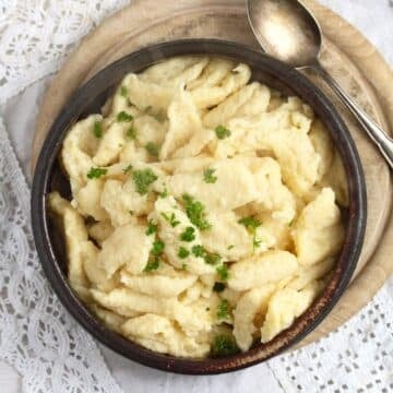 overhead image of nokedli in a brown bowl with a spoon on a wooden board.