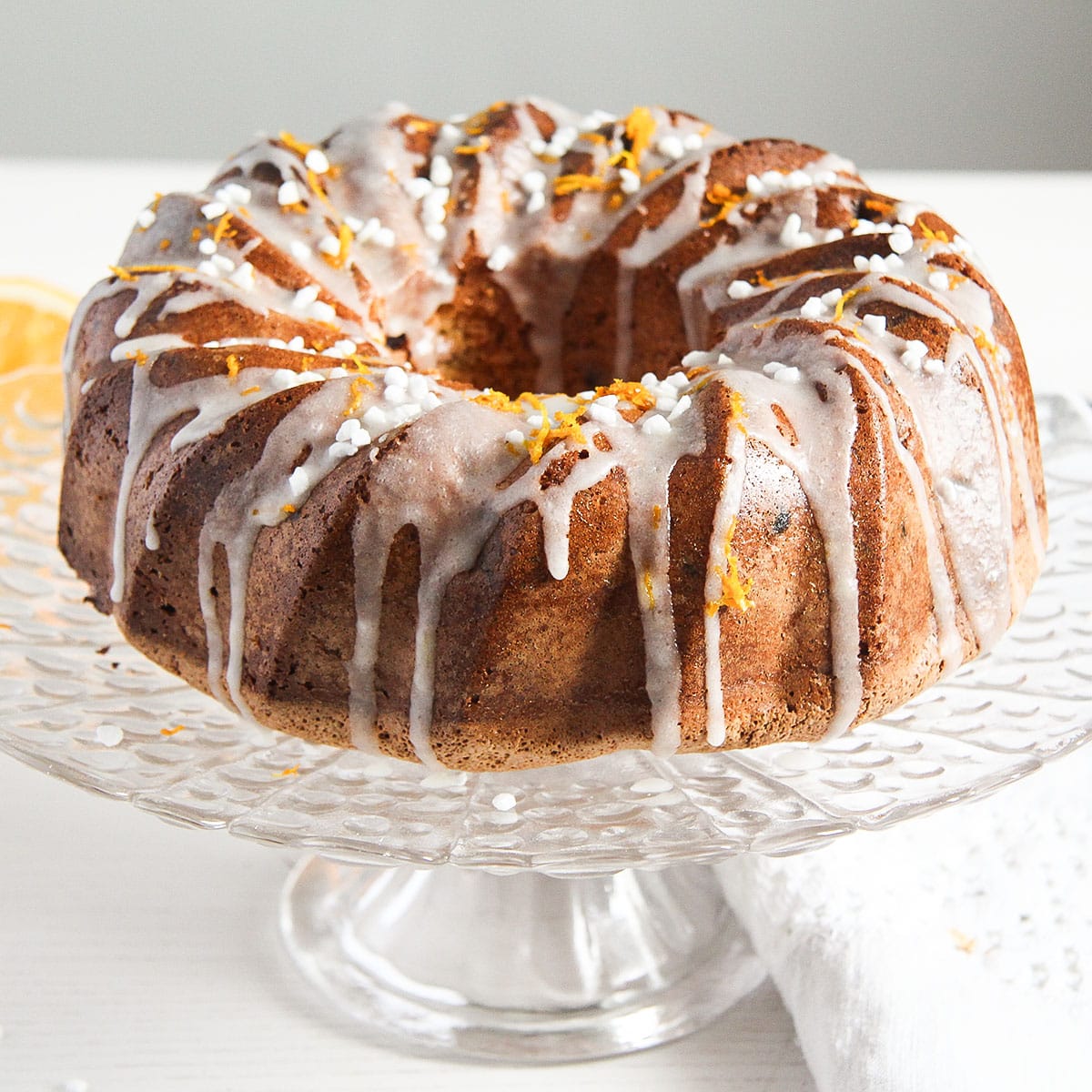 orange raisin cake drizzled with orange glaze on a cake platter.