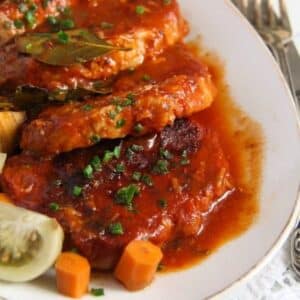 sliced pork in tomato sauce served with pickles on a platter.