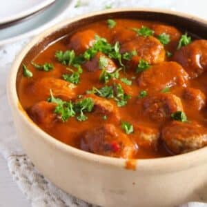 small pot full of pork meatballs in tomato sauce with parsley.