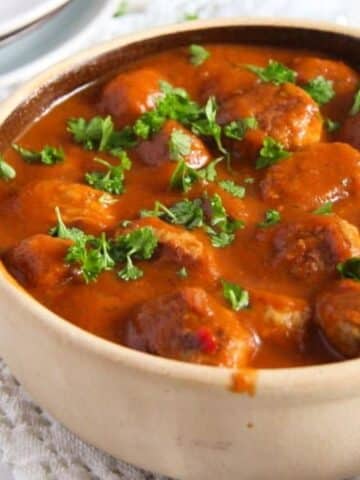 small pot full of pork meatballs in tomato sauce with parsley.