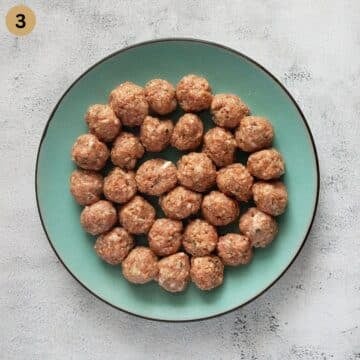 many small uncooked meatballs on a blue plate.