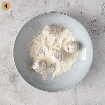 coating small meatballs with flour on a plate.