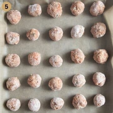 many unbaked pork meatballs on a baking sheet.