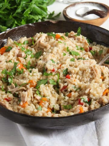 romanian chicken pilaf in an large brown bowl with parsley and bowl of salt behind it.