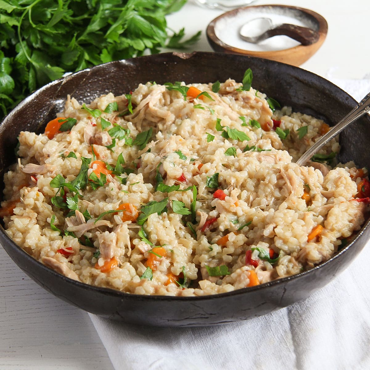 romanian chicken pilaf in an large brown bowl with parsley and bowl of salt behind it.
