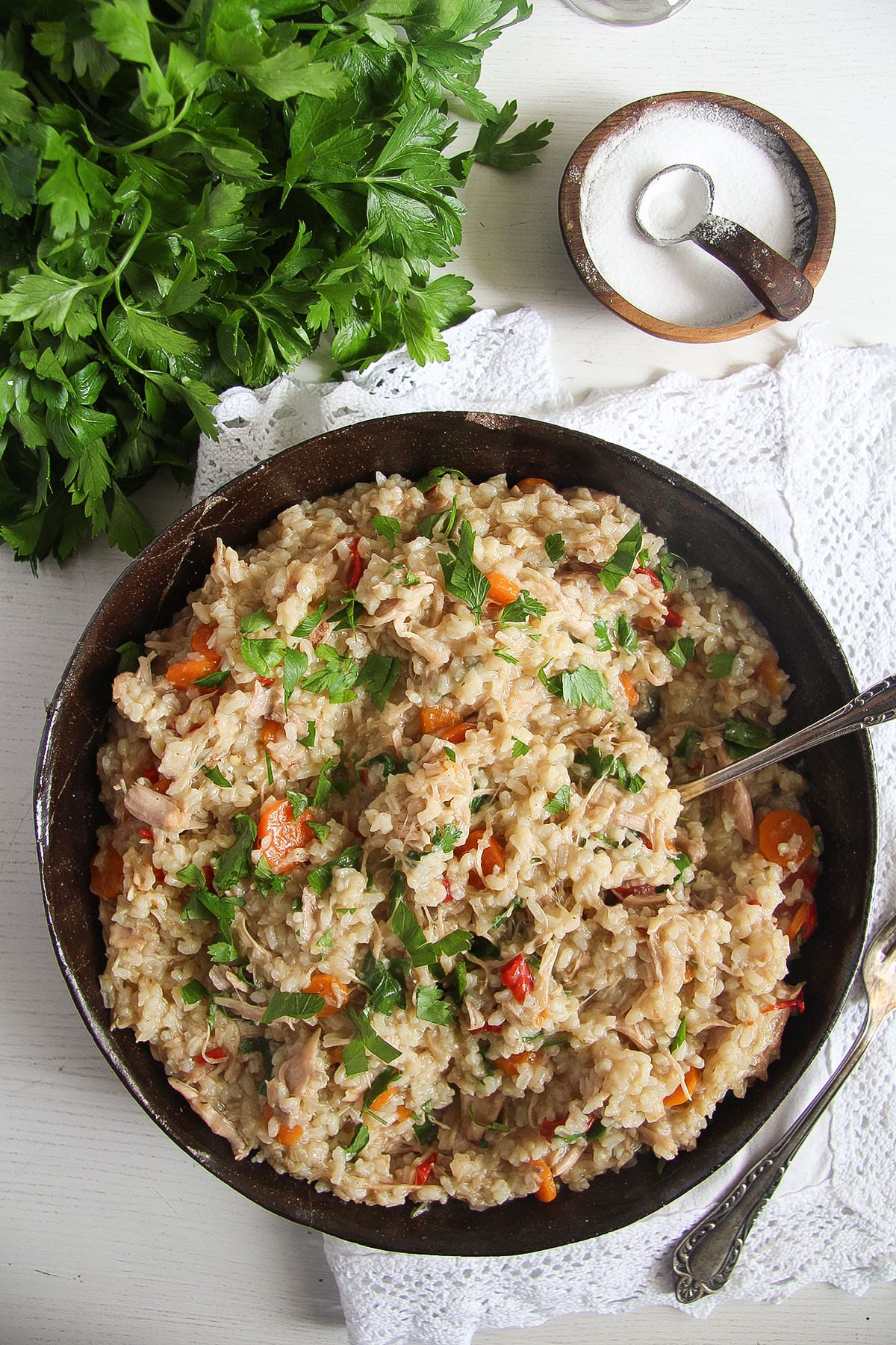 a bowl with romanian pilaf with chicken, fresh parsley and a bowl of salt near it.