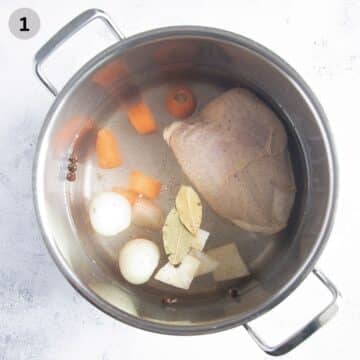 a whole, bone-in chicken breast, chopped carrots and onions covered with water in a saucepan.
