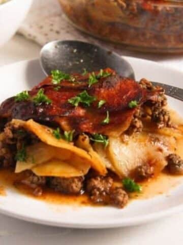 romanian moussaka with potatoes, ground pork and tomatoes served on a plate.