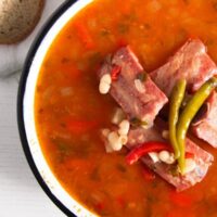 small ribs on top of a bowl or red soup with white beans
