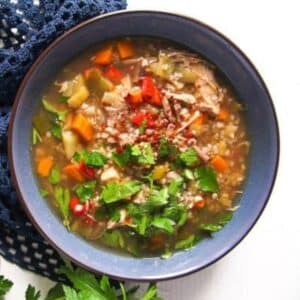 buckwheat soup with vegetables and parsley in a blue bowl.