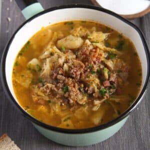 german pork and cabbage soup in a small green pot.