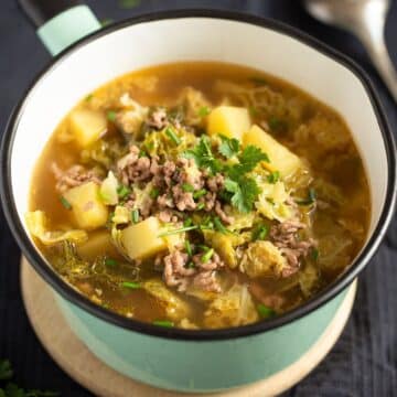 german savoy cabbage soup with ground meat and potatoes in a small, green serving saucepan.