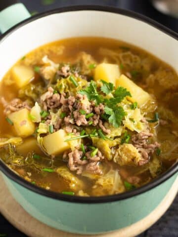 german savoy cabbage soup with ground meat and potatoes in a small, green serving saucepan.