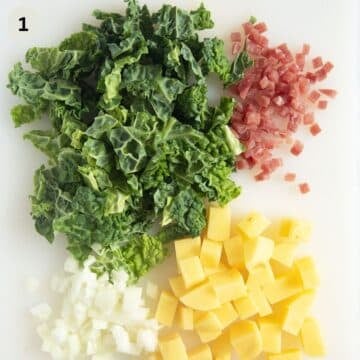 chopped savoy cabbage, onion, potatoes, and bacon cubes on a cutting board.