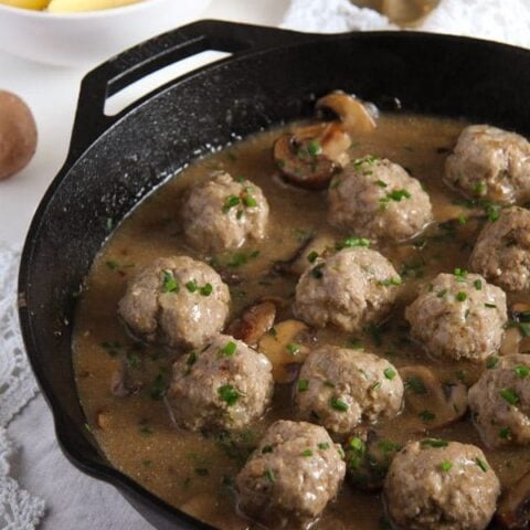 polish meatballs simmered in a cast-iron skillet with mushrooms
