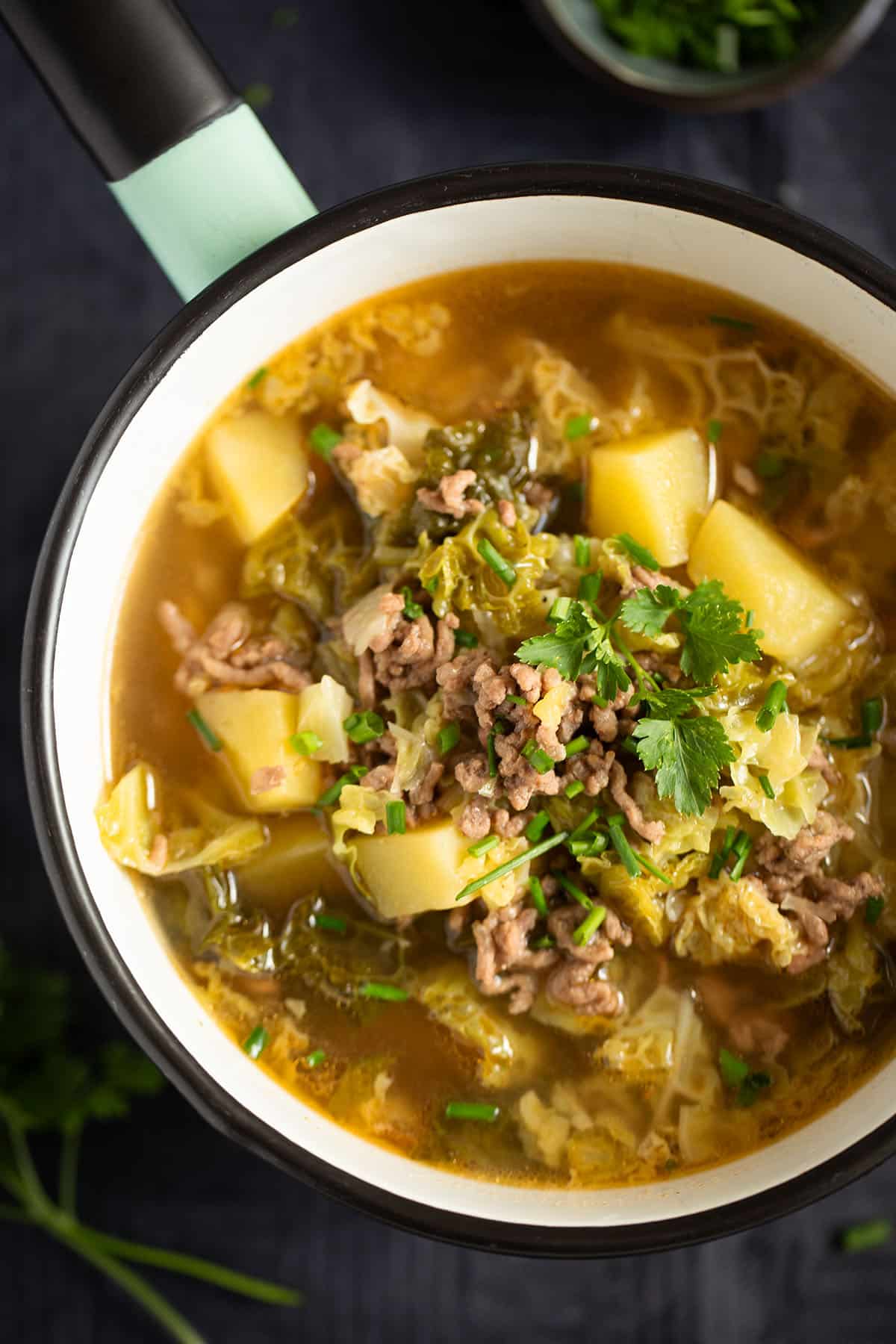 a small saucepan full of soup with savoy cabbage, potatoes, and ground beef.