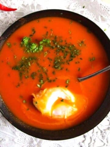 black bowl with red tomato soup, green parsley and a poached egg.