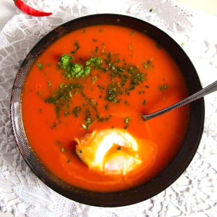 black bowl with red tomato soup, green parsley and a poached egg.