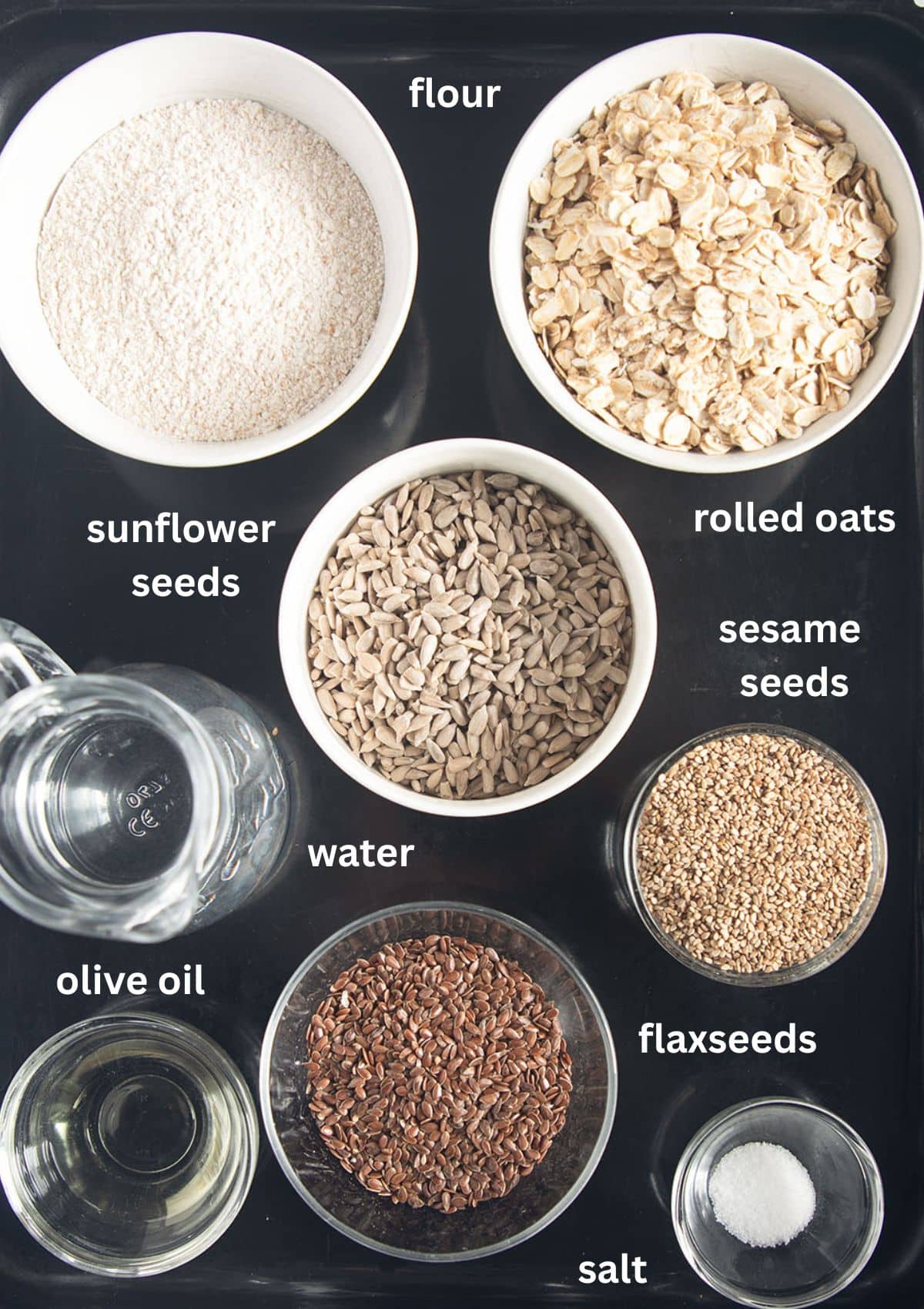 labeled ingredients for making crispbread with rolled oats, flour, sunflower seeds, flaxseeds, and sesame seeds.