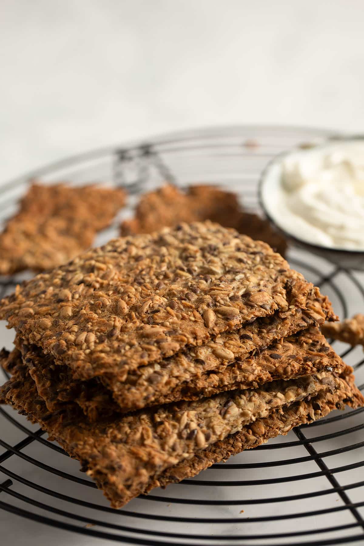 several pieces of homemade crispbread on a wire rack with a small bowl of dip behind it.