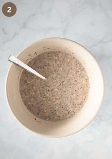 oats. flour, seed and water mixture for making crispbread in a bowl with a spoon in it.