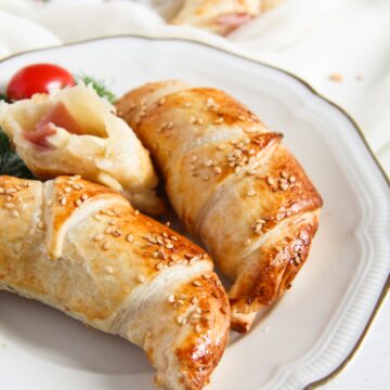 two and half puff pastry croissants stuffed with ham and cheese on a plate.