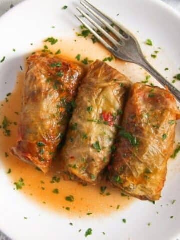 three cabbage rolls on a small white plate with a bit of sauce and a fork.