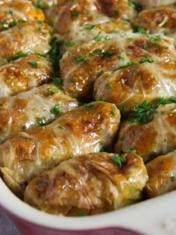 many golden vegan stuffed cabbage rolls in a baking dish.