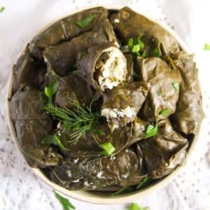 overhead view of many vegetarian dolma rolls in a bowl and sprinkled with dill.