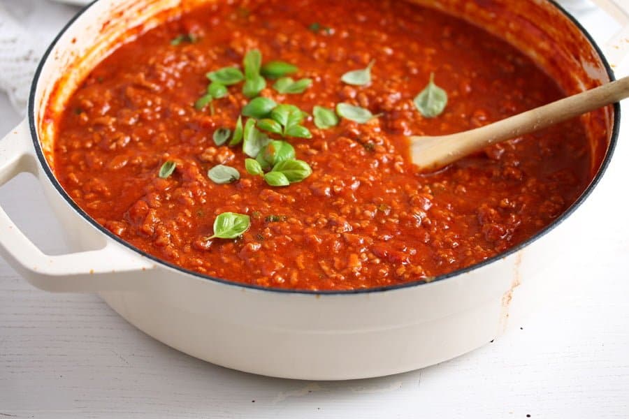 red meat sauce sprinkled with basil in a white cooking dish