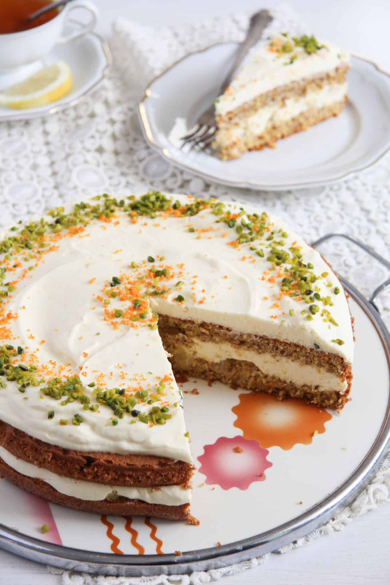 layered carrot cake with almonds and orange cream filling on a platter and a slice behind it.
