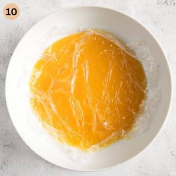orange filling for cake with a piece of cling film on top in a bowl.