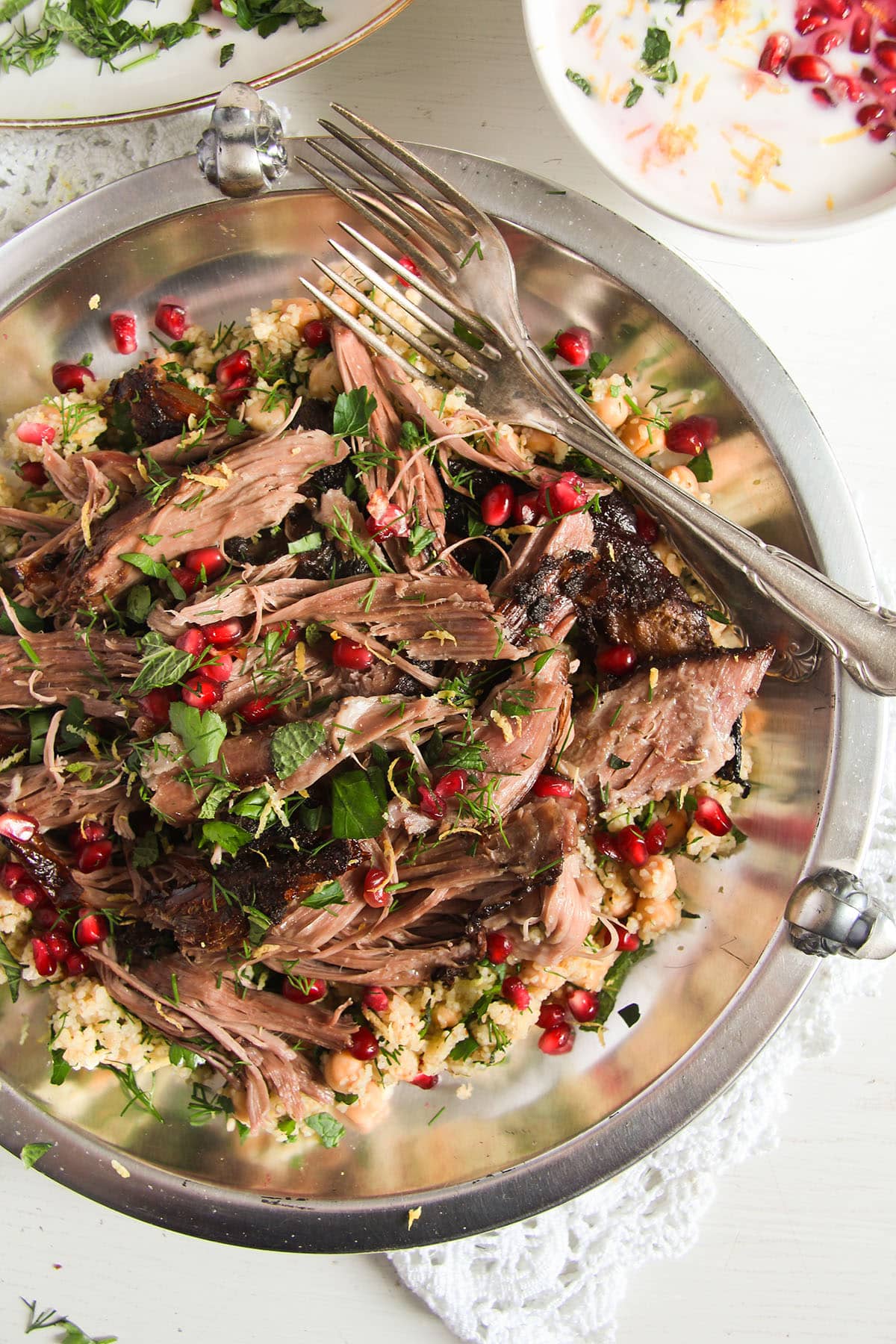 shredded pomegranate lamb and two forks on a large plate.