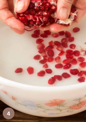 hands adding pomegranate seeds to a bowl of yogurt.
