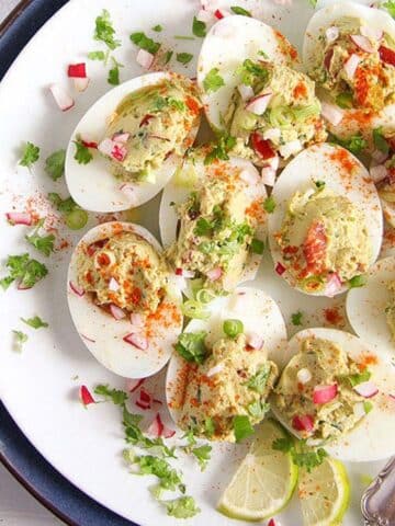 mexican deviled eggs sprinkled with cilantro and served with lime wedges.