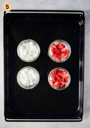 four dessert cups, two showing crushed meringue and two chopped strawberries.