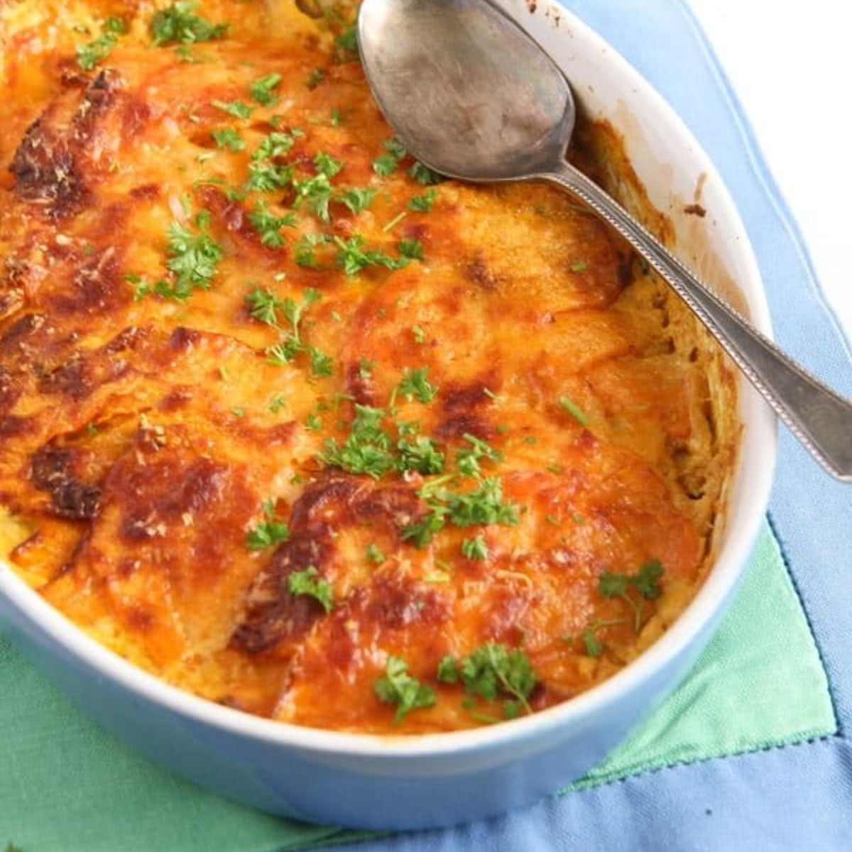 sweet potato dauphinoise in a small blue dish on a green cloth.