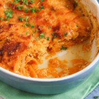 scooped out sweet potato gratin in a blue baking dish on a green towel.