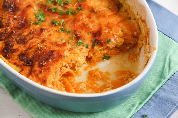 scooped out sweet potato gratin in a blue baking dish on a green towel.