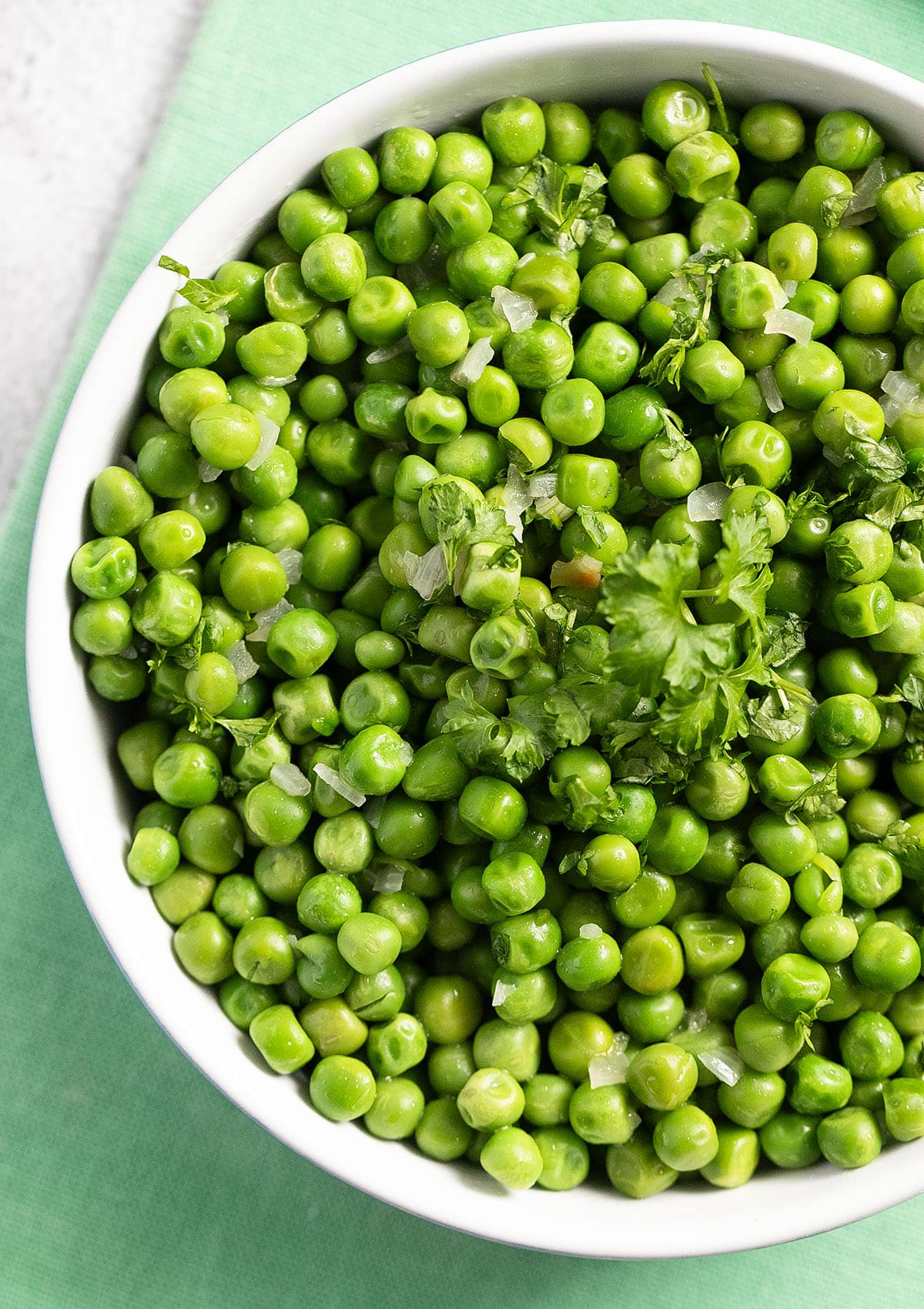close up of a bowl of vibrant green peas cooked in butter.