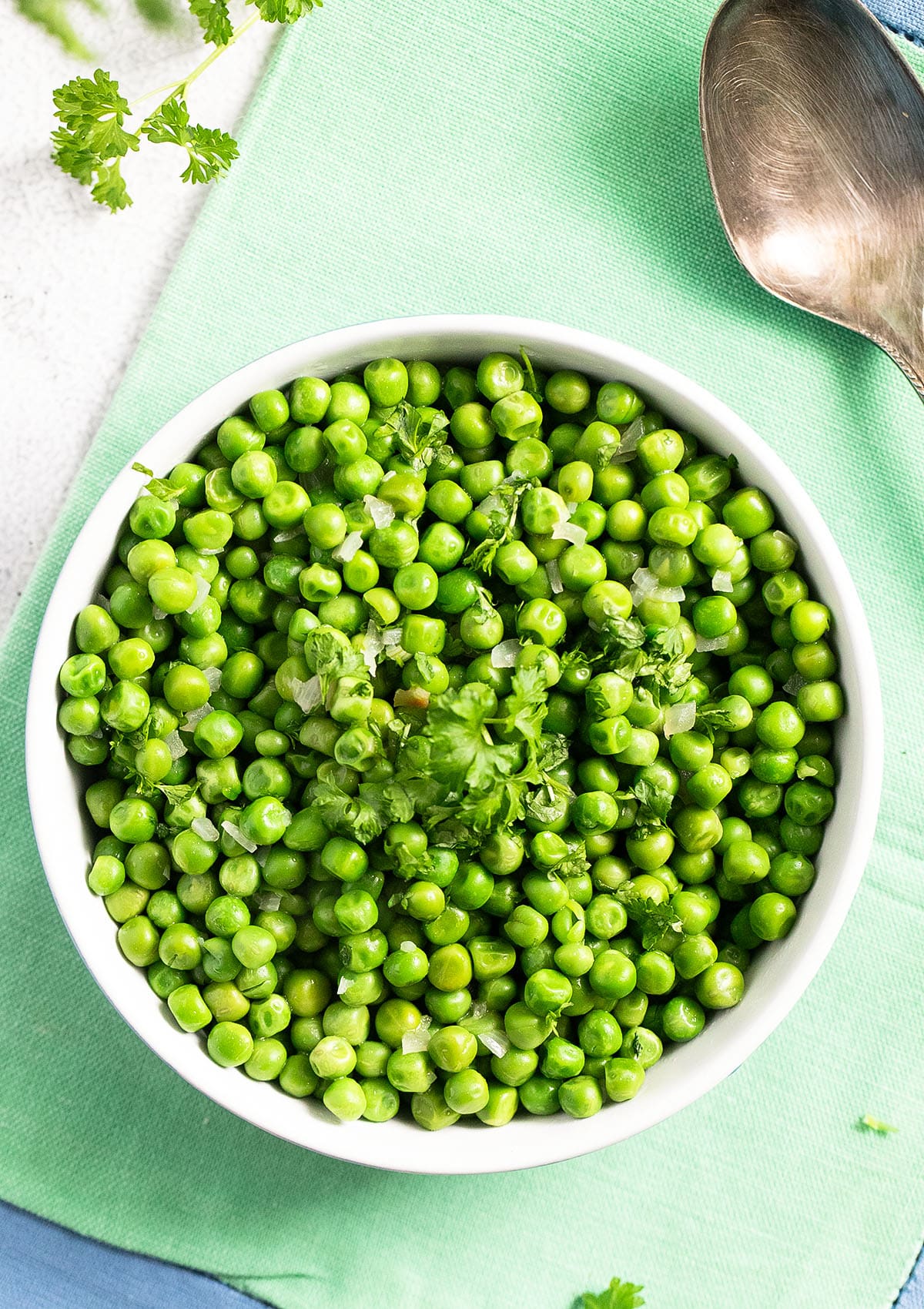 buttered peas sprinkled with parsley in a bowl on a green cloth.